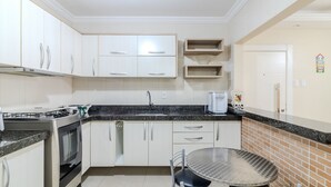 A modern kitchen with white cabinets, a stainless steel oven, a granite countertop, and a round dining table with chairs. - 2BR Full apt Beachfront Ese0102 (Balneário Camboriú)