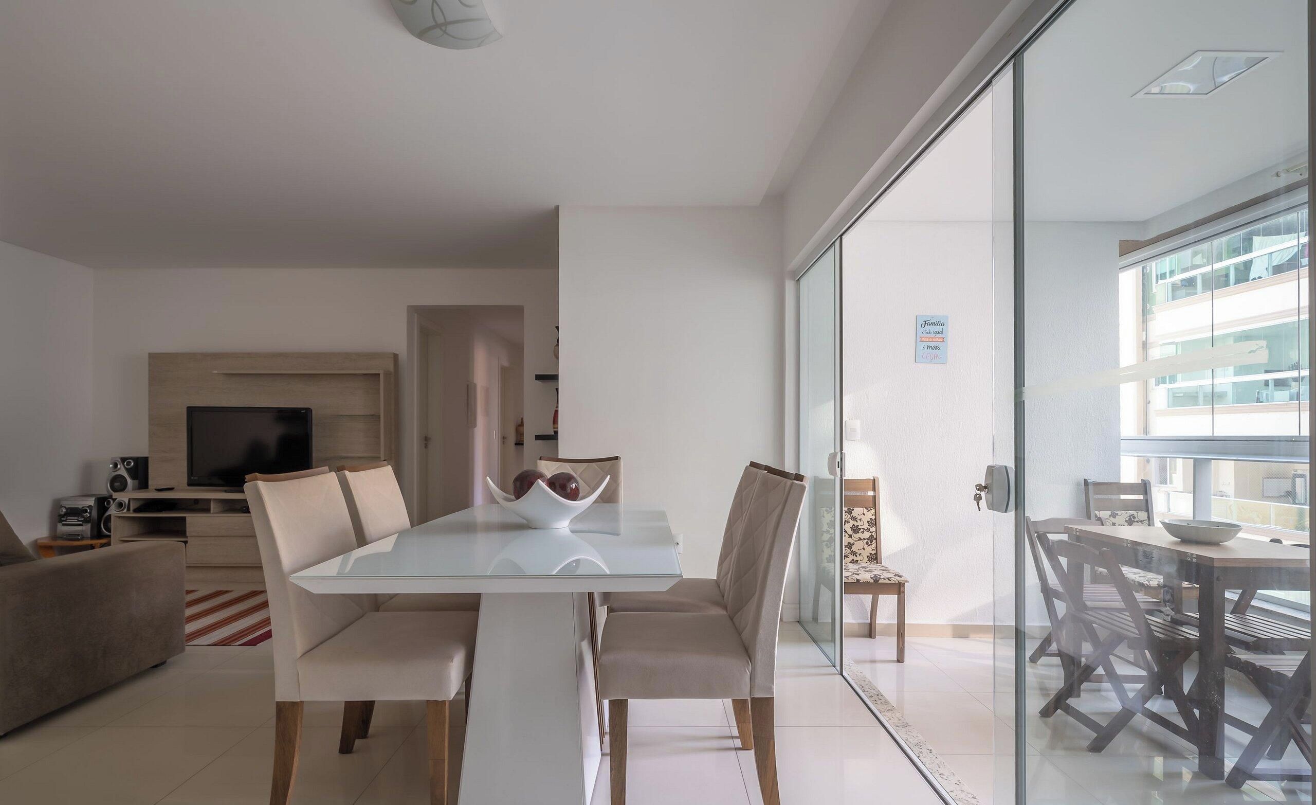Una sala de estar moderna con una mesa de comedor de vidrio, asientos cómodos, un televisor de pantalla plana y una cocina al fondo.