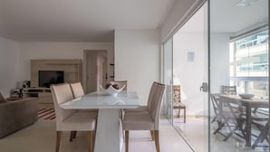 A modern living room with a glass dining table, beige sofas, and a TV on a wooden stand. - 3BR apt w/ Bbq, 500m From Beach Itapema Esm602 (Itapema)