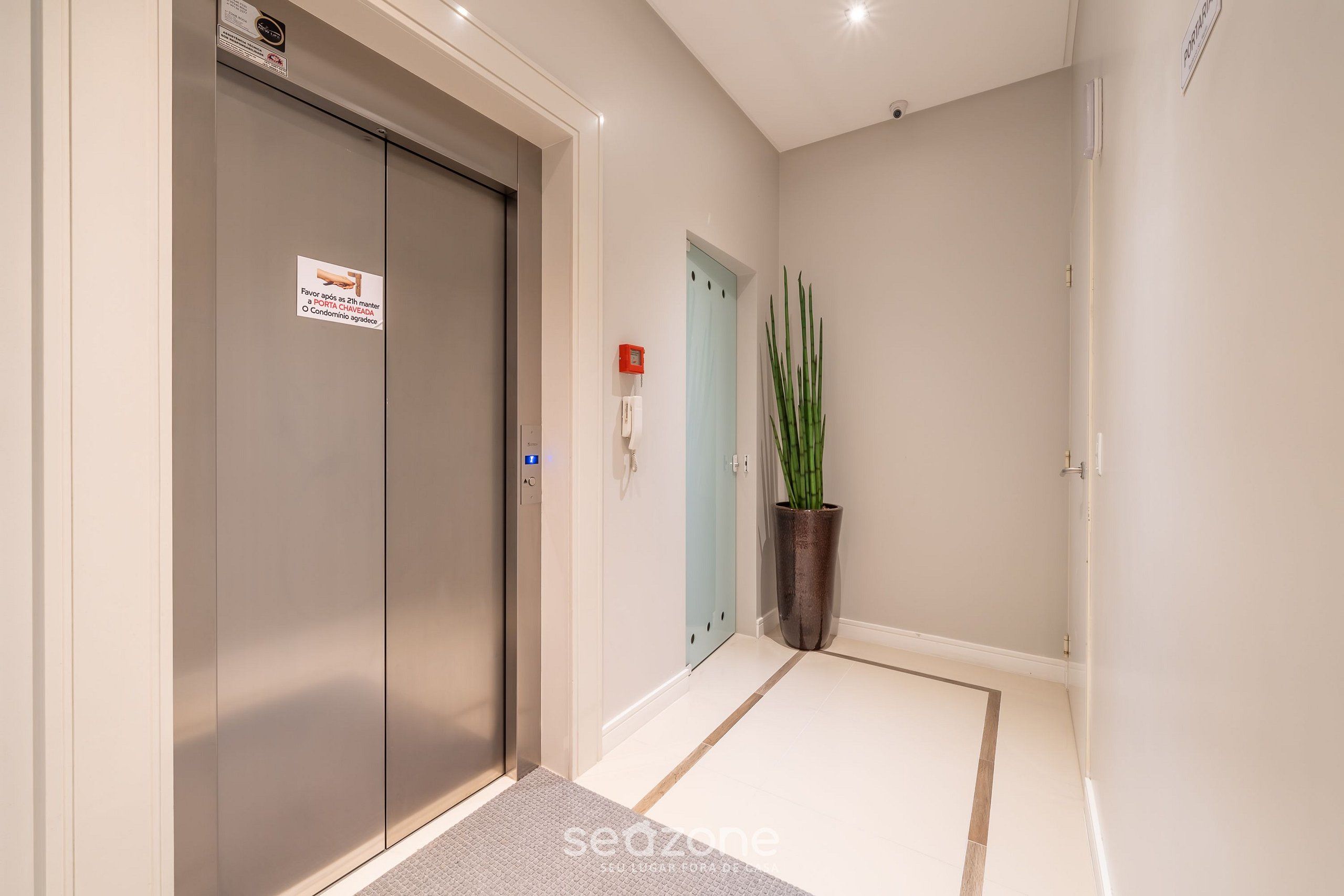 A hallway with a modern elevator, a potted plant, and a door with a light switch.