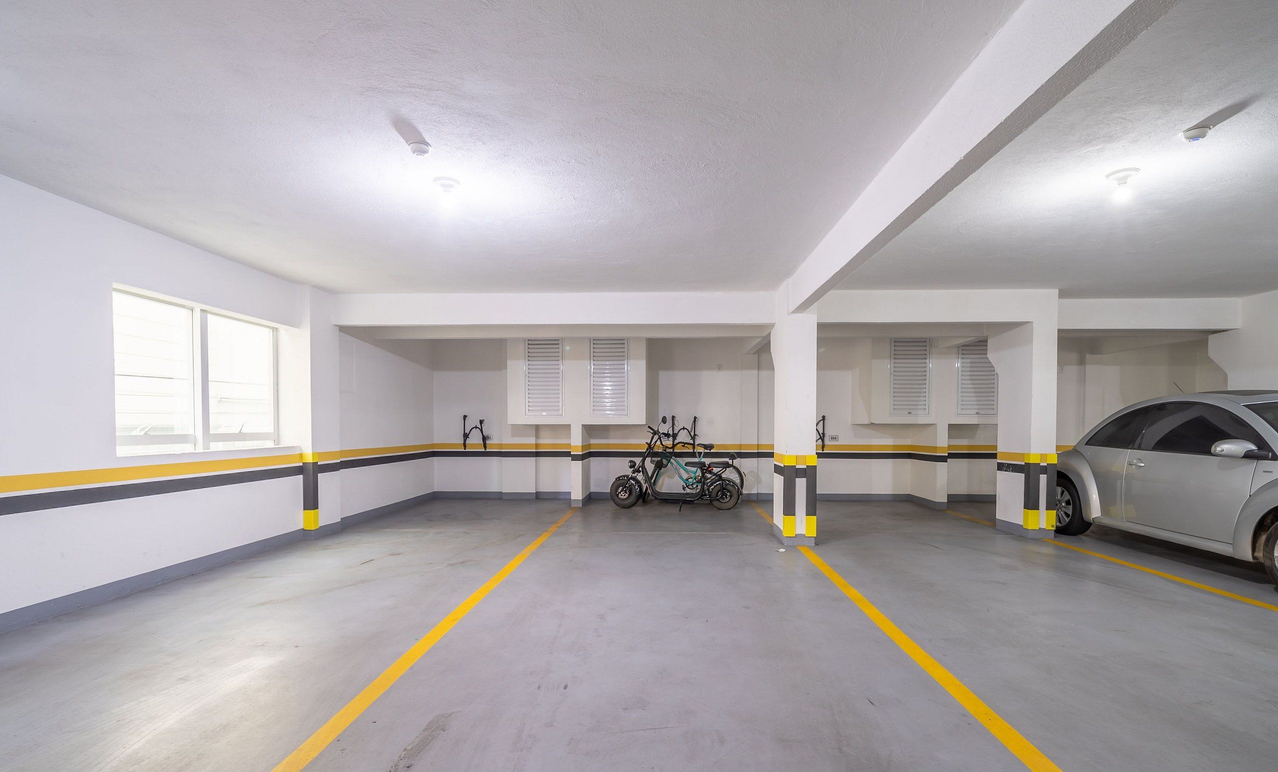 Un parking aux murs blancs, aux lignes rayées jaunes et noires, et où une voiture est garée sur le côté droit.