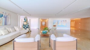 Un moderno vestíbulo de hotel con un sofá blanco, dos sillones, una mesa de centro de vidrio y un árbol de Navidad.