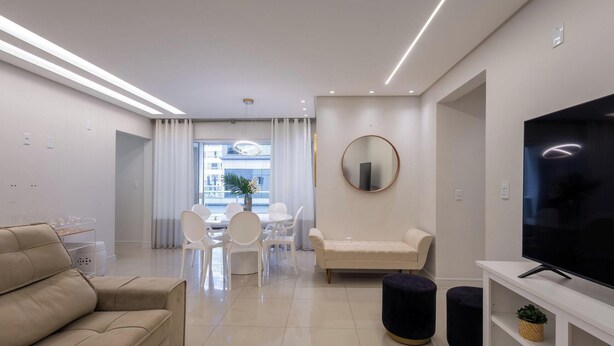 A modern living room with a sofa, TV, and dining area with chairs and a table.