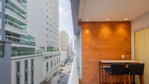 A balcony with a table and chairs, overlooking a city street with buildings and parked cars.