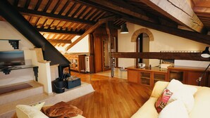 Ruime loft met houten balken, een open haard, een keukenhoek en een gezellige zithoek met kussens.