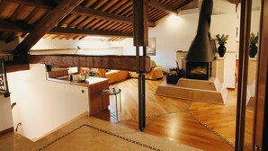 Een ruime loft met zichtbare houten balken, een open haard en een gezellige zithoek.
