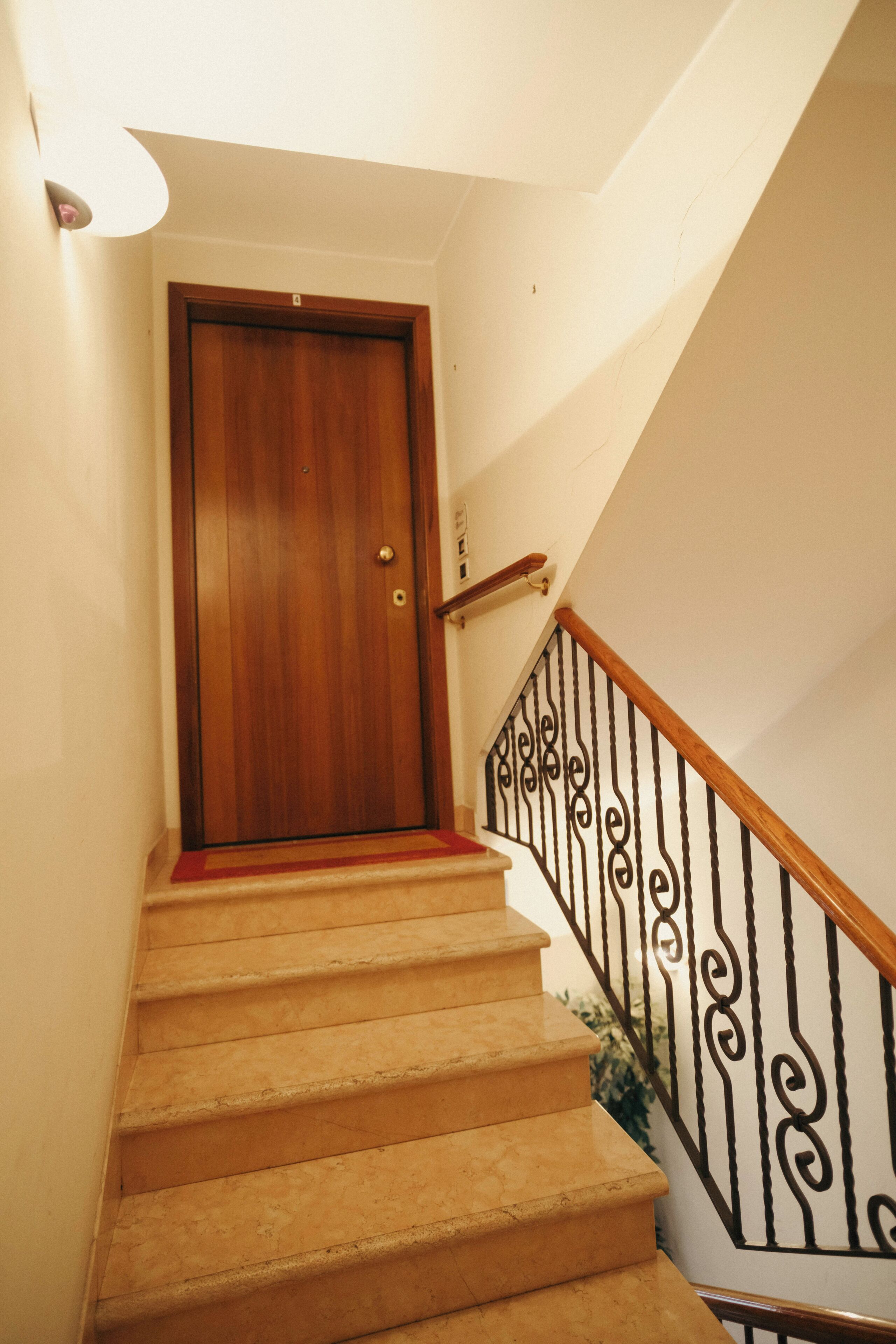 Une porte en bois, située en haut d’un escalier recouvert de moquette et muni d’une rampe en métal noir.