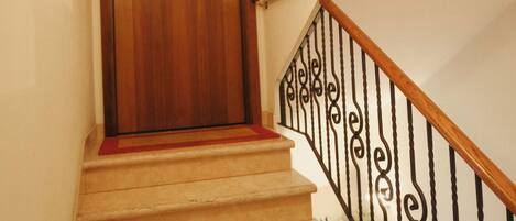 Une porte en bois, située en haut d’un escalier recouvert de moquette et muni d’une rampe en métal noir.