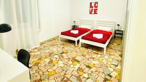 A room with two beds, a white air conditioner, a ceiling light, and a mosaic floor. - Ama Cagliari (Cagliari)