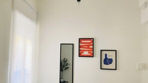 A room with a large window, a black chair, a potted plant, and three framed pictures on the wall. - Ama Cagliari (Cagliari)