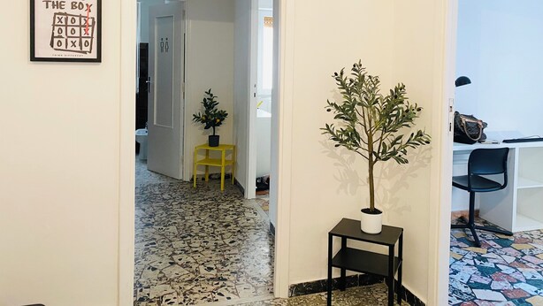 A hallway with a tiled floor, a potted plant, a small table, and a framed motivational quote on the wall. - Ama Cagliari (Cagliari)