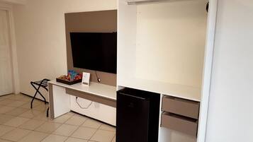 Una habitación con un escritorio blanco, un refrigerador negro y un televisor en la pared.
