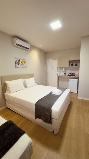 Une chambre d’hôtel avec un lit, une petite kitchenette et un appareil de climatisation blanc.