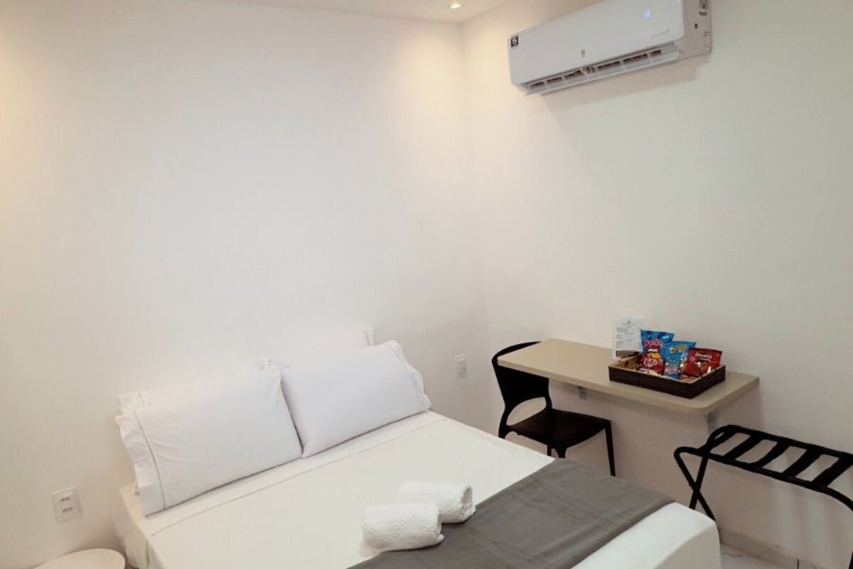 Une chambre d’hôtel équipée d’un lit, d’un bureau, d’une chaise, d’un climatiseur et d’une petite table.