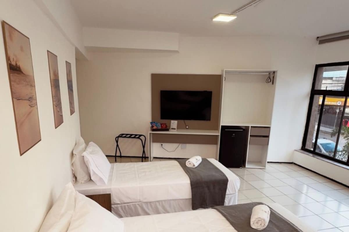 Une chambre d’hôtel avec deux lits, une télévision, un bureau et une fenêtre.
