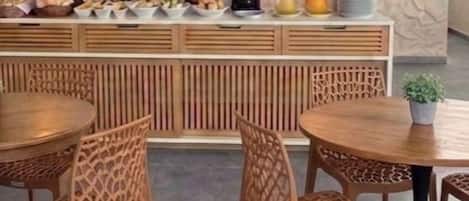 A dining area with round tables and chairs, a buffet with various food items, and decorative wall sconces.