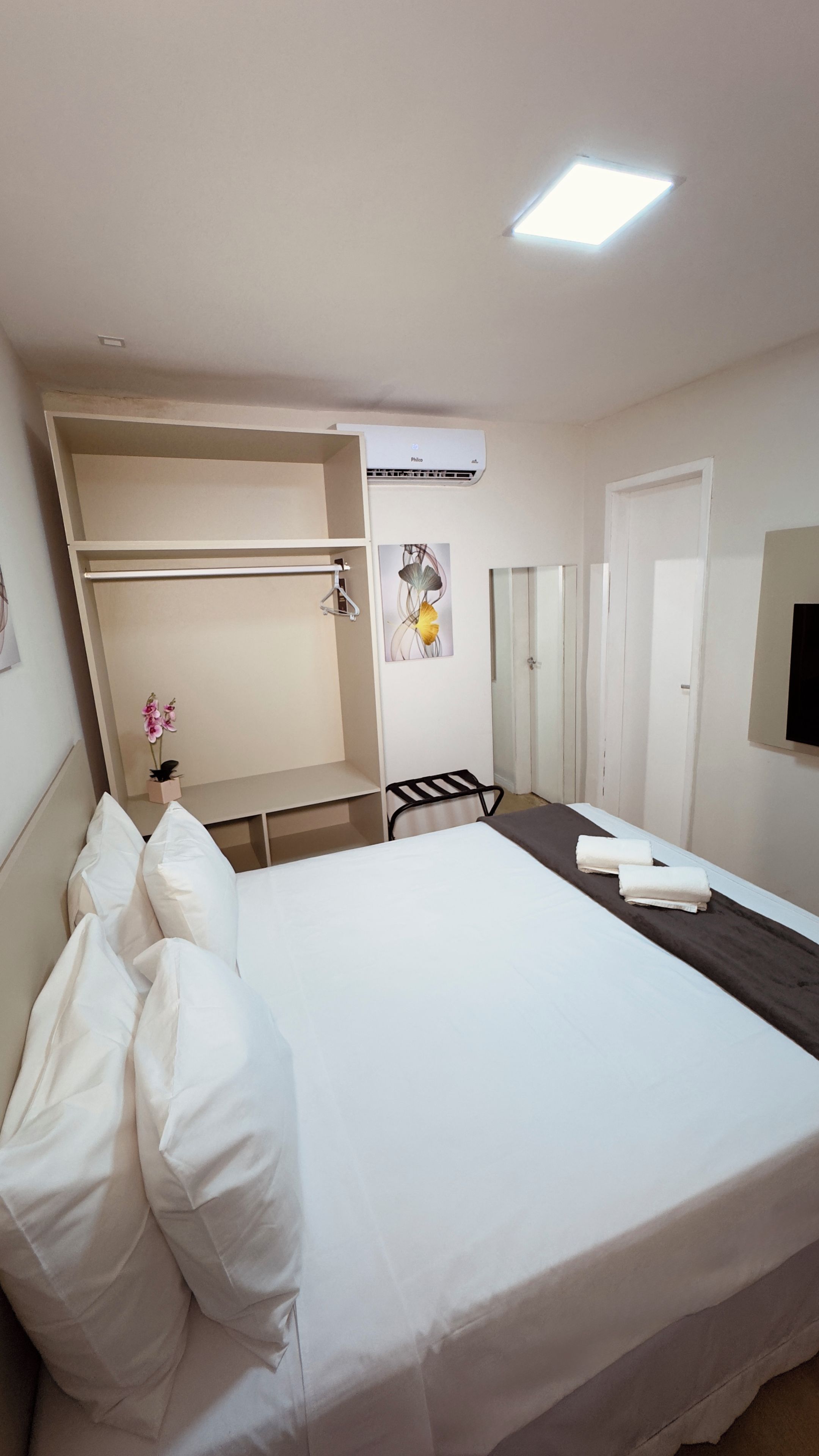 Ein Hotelzimmer mit Bett, Schreibtisch, Stuhl, Kleiderschrank, Klimaanlage und einer kleinen Topfpflanze.