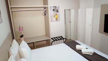 Een hotelkamer met een bed, een bureau, een stoel, een kledingkast, een airconditioning en een kleine kamerplant.