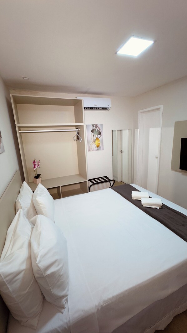 A hotel room with a bed, a desk, a chair, a wardrobe, an air conditioning unit, and a small potted plant. - Hotel Vistta Iracema (Fortaleza)