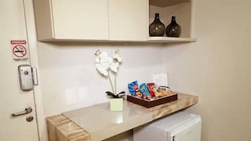 A compact kitchenette with a marble countertop, a small refrigerator, and a shelf with decorative items.
