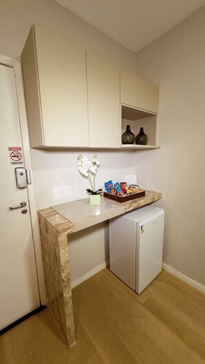 Une petite cuisine équipée avec un plan de travail en marbre, un petit réfrigérateur et une étagère ornée d’objets décoratifs.