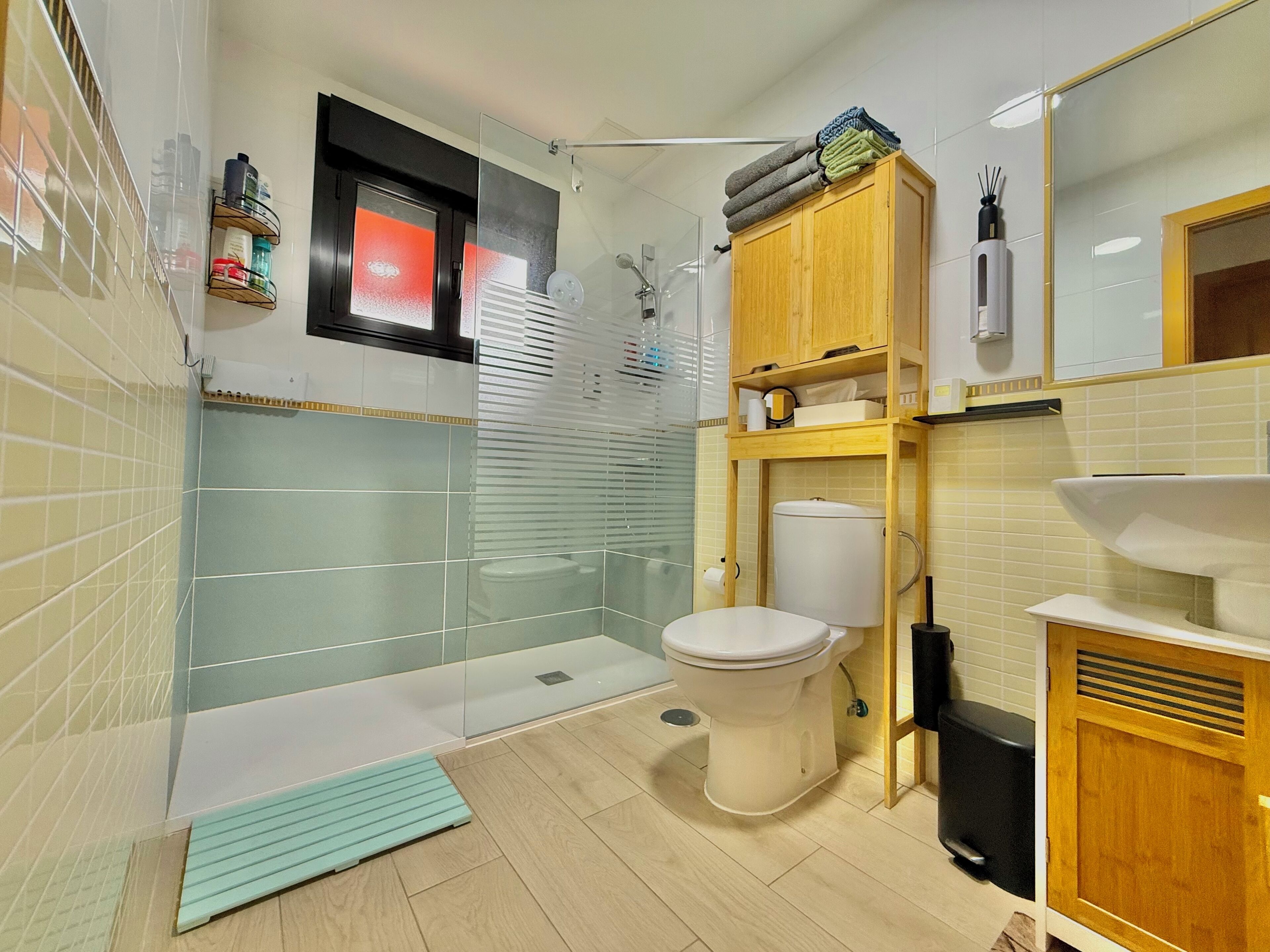 Un baño moderno con cabina de ducha de vidrio, inodoro, lavabo y un armario de madera con toallas.