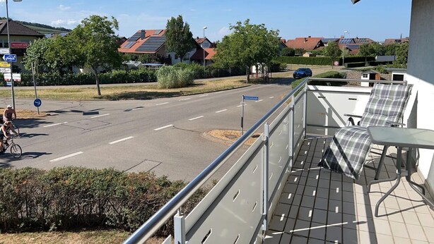 En balkon med udsigt over en boligvej, en cyklist og en parkeret bil.