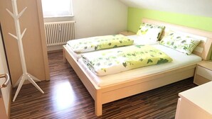 Et soveværelse med skråvæg, radiator, trægulv og en seng med blomstret sengetøj.