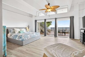 Un dormitorio con cama, ventilador de techo, ventana grande y vista al exterior.