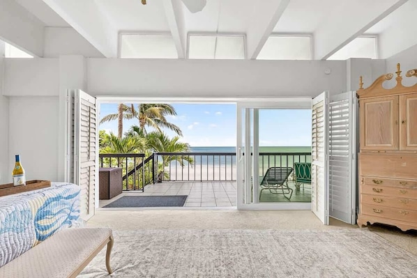 A bedroom with a large sliding glass door leading to a balcony with a view of the beach and palm trees.