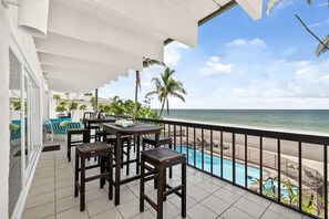 A balcony with a pool view, outdoor seating, and a clear sky.