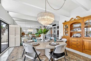A modern dining room with a round table, chairs, a chandelier, and a wooden cabinet with glass doors. - Casa Bella – A Coastal Dream with Panoramic Views (Redington Beach)