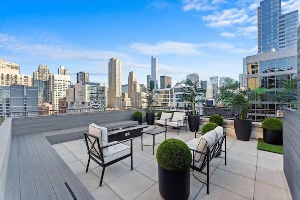 A rooftop terrace with outdoor seating, potted plants, and a city skyline view.