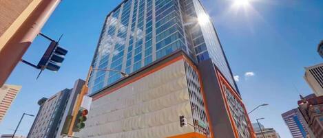 A modern high-rise building with a glass facade, surrounded by other buildings and a clear sky.
