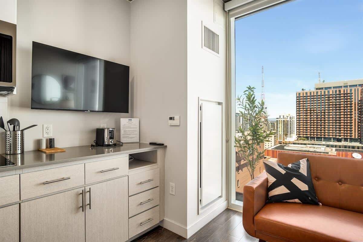 A modern kitchen with a flat-screen TV, a coffee maker, and a view of the city through a large window.