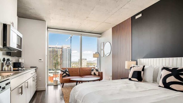 A modern hotel room with a large bed, a sofa, a dining area, and a view of the cityscape. - Boulevard Stays Sleek Studio Pool, Gym, & Paid Parking (Phoenix)
