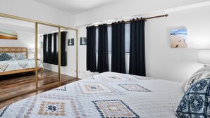 A bedroom with a bed, a mirror, a window with curtains, and a painting on the wall.
