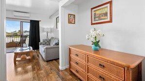 A modern living room with a sofa, a wooden cabinet, and a glass coffee table. There is a balcony with a view of the city.