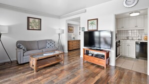 A living room with a sofa, coffee table, TV, and kitchen area with cabinets and appliances.