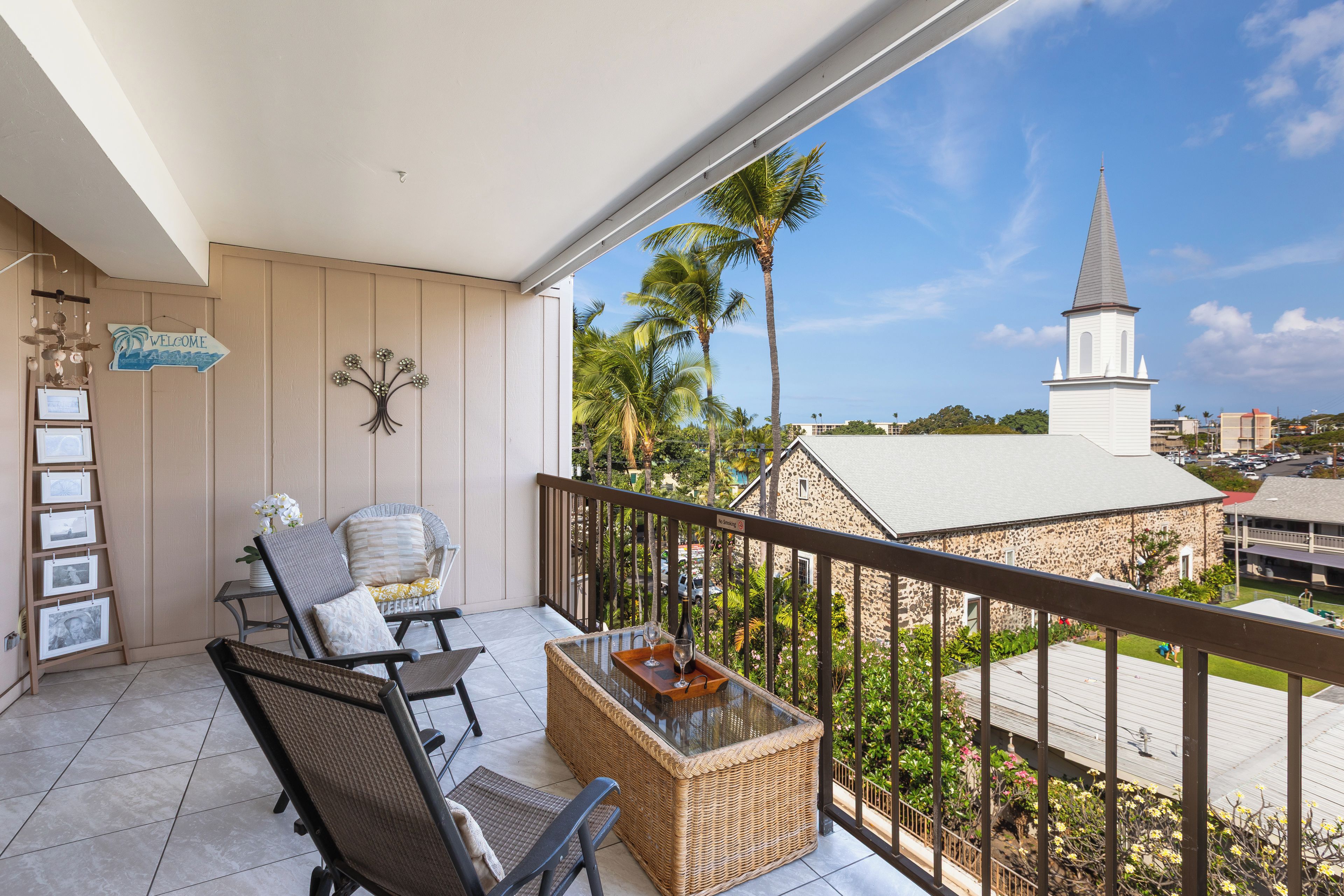 A balcony with wicker furniture, a welcome sign, and a view of a church and surrounding buildings.