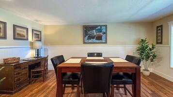 A dining area with a wooden table, four chairs, a lamp, and framed artwork on the wall.