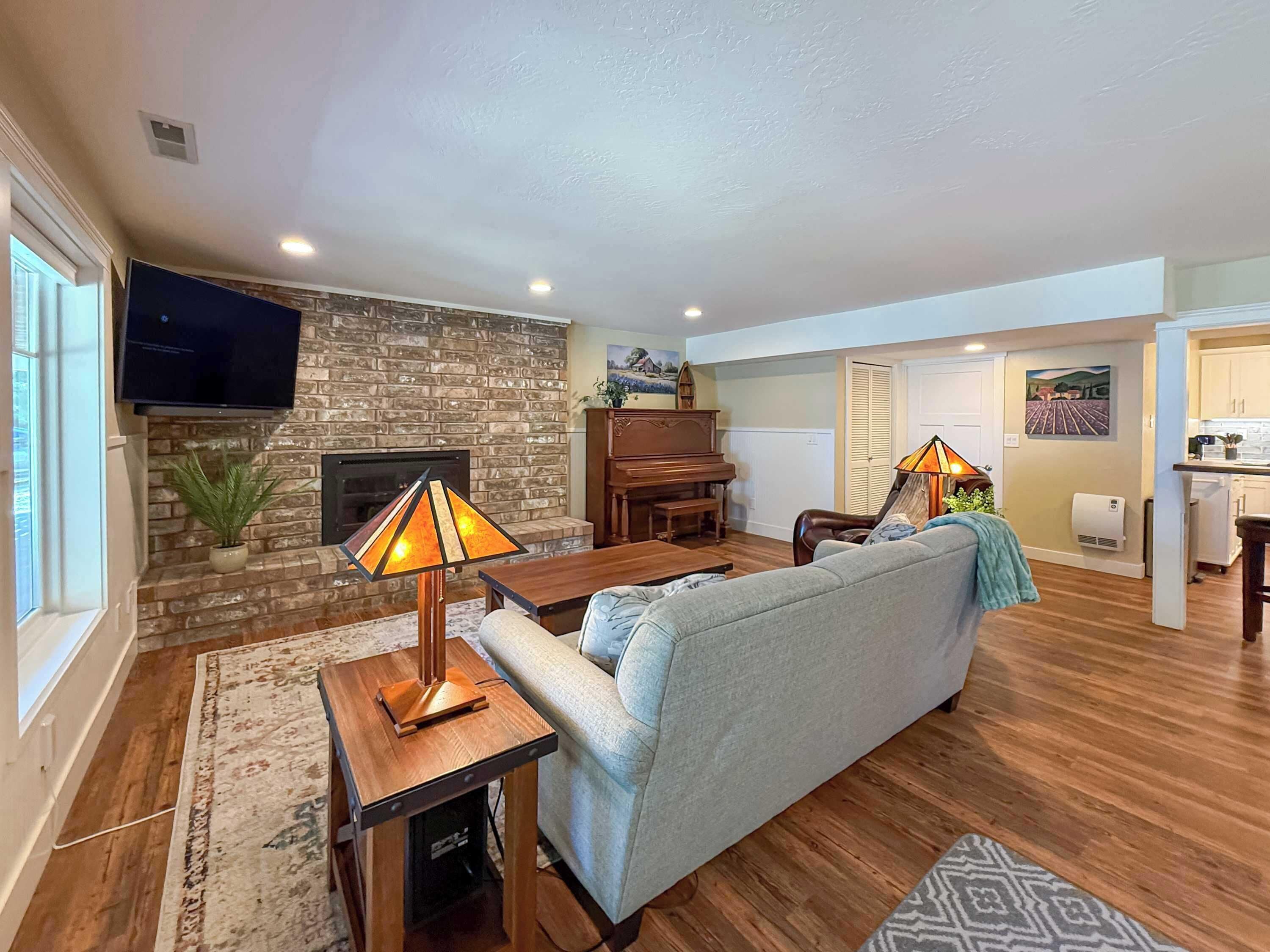A living room with a stone fireplace, a television, a piano, and a sofa.