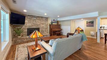A living room with a stone fireplace, a television, a piano, and a sofa.