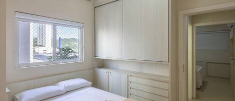 A bedroom with a bed, a window, a wardrobe, and a bathroom visible through an open door.