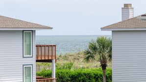 A beachfront property with a wooden deck overlooking the ocean, white siding houses, and a palm tree.