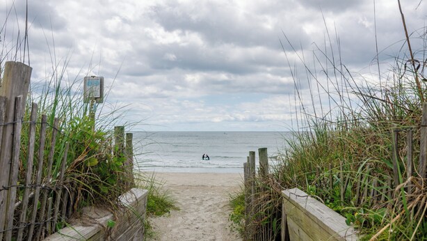 A beach path leading to the sea with a wooden fence and a signpost.