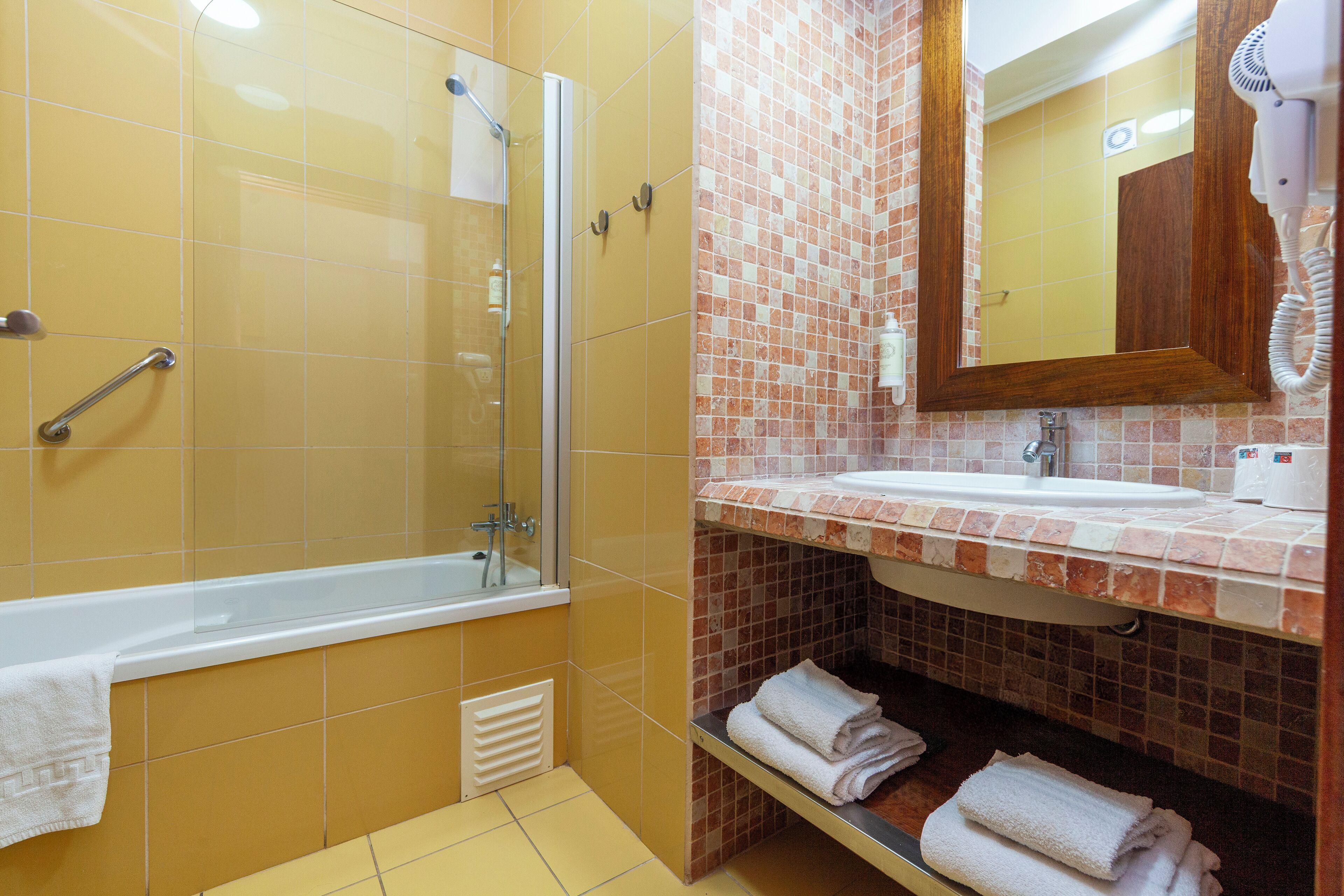 Een badkamer met een douche met glazen wand, een wastafel met spiegel en een handdoekrek.