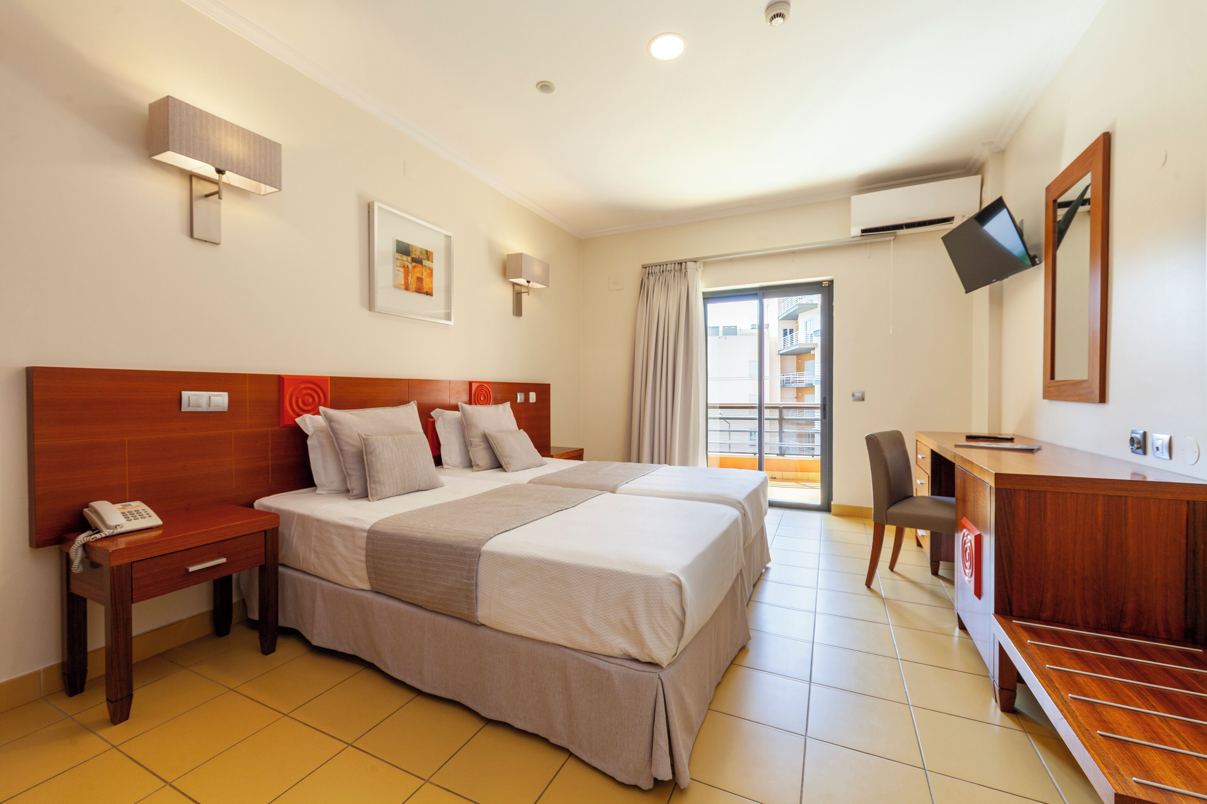 A hotel room with a large bed, bedside tables, a desk, and a TV.