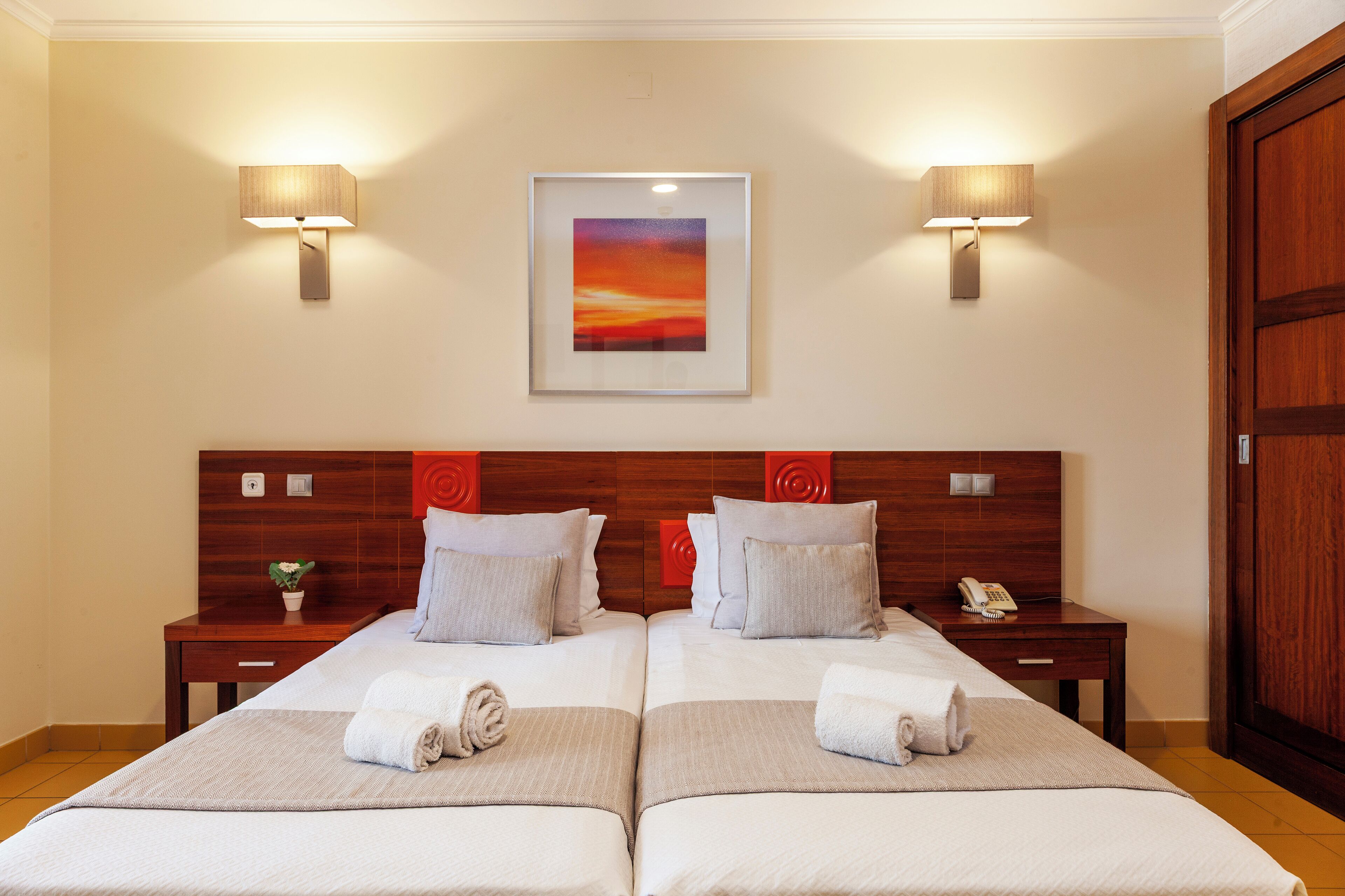Ein Hotelzimmer mit zwei Betten, einem gerahmten Kunstwerk darüber und zwei Nachttischlampen.