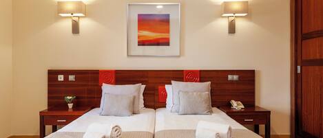 A hotel room with two beds, a framed artwork above, and two bedside lamps.
